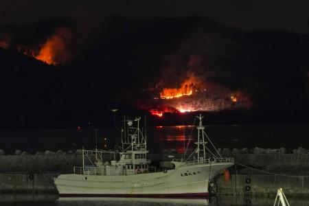 　延焼が続く岩手県大船渡市三陸町綾里の山林火災現場。手前は三陸町越喜来の崎浜漁港＝４日午後６時３０分（１秒露光）