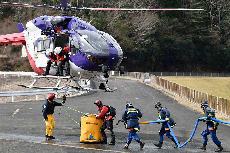 ホバリングした県防災ヘリにつるしたバケットへの注水に向かう団員＝大垣市上石津町打上、水嶺湖畔